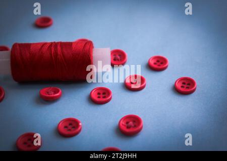 Beautiful texture with lots of round red buttons for sewing, needlework and a coil of thread. Copy space. Flat lay. Blue background. Stock Photo