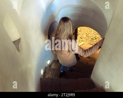 A girl, a woman descends the steep stone spiral stairs going down the narrow steps. Stock Photo