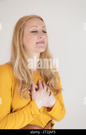 Portrait of confident beautiful woman with long brown hair, wearing casual clothes, standing in relaxed pose with hands on chest, breathing deeply, doing breathing exercise. Stock Photo