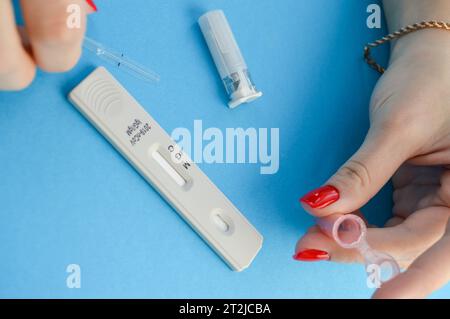 a pink plastic container for blood collection. a girl with a red manicure holds a small form for taking blood in her hands and is about to pierce her Stock Photo