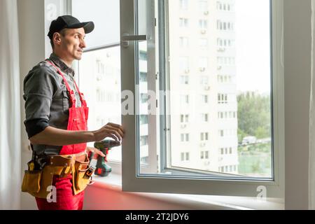 Worker installs windows master sverdit frame to attach to the base repair in high-rise building Stock Photo