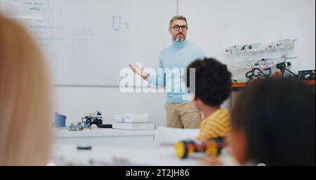 Science, learning and teacher with children in classroom for research on project in school. Knowledge, education and man educator or tutor helping kid Stock Photo