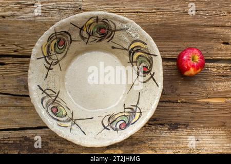 empty bowl and fresh apple on wooden background - handmade pottery Stock Photo