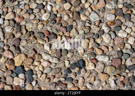 Full frame abstract macro texture background of an old aggregate walking surface with exposed stones and pebbles in bright sunlight Stock Photo