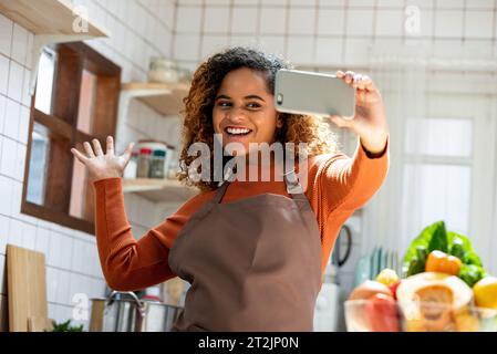 Happy African American lady using cellphone during online class in blurred background of the kitchen Stock Photo