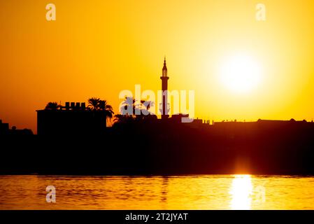 View across large wide river Nile in Egypt through rural countryside landscape with beautiful orange sunset and mosque minaret architecture Stock Photo