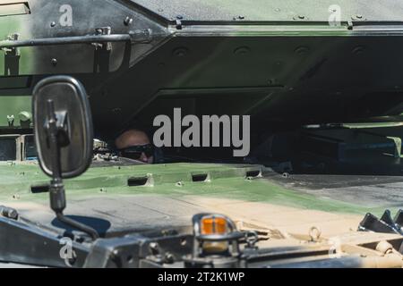 16.08.2023 Warsaw, Poland. Bald soldier in sunglasses hiding inside military tank. Various camouflage options during open-air fight. High quality photo Stock Photo