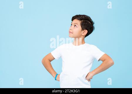 Handsome mixed race boy thinking and looking up with arms akimbo in isolated studio light blue color background Stock Photo