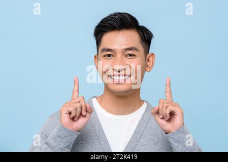 Handsome southeast Asian man smiling and pointing hands up in isolated studio light blue color background Stock Photo