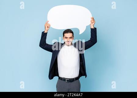 Portrait of young handsome Caucasian man in formal dress holding speech bubble on isolated light blue studio background Stock Photo