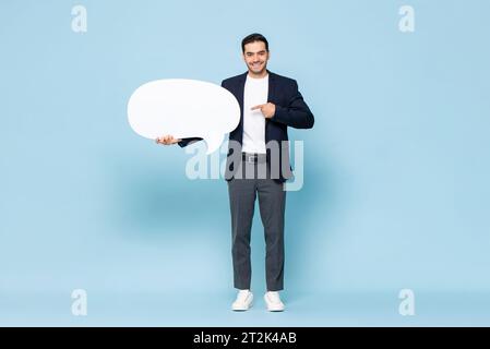 Portrait of young handsome Caucasian man in formal dress holding speech bubble on isolated light blue studio background Stock Photo