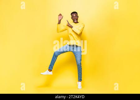 Shocked African man jumping with hands raised in studio yellow color isolated background Stock Photo