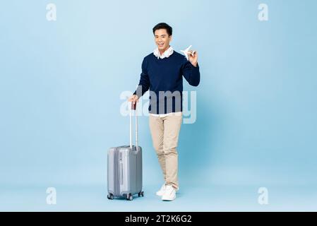 Young smiling handsome Asian tourist man with baggage, passport and boarding pass ready to fly Stock Photo