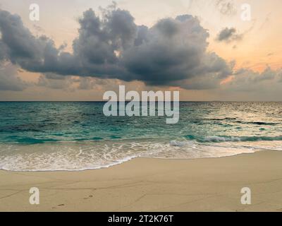 Dramatic dark storm clouds moving onto a beautiful clean sandy beach at sunset. Stock Photo