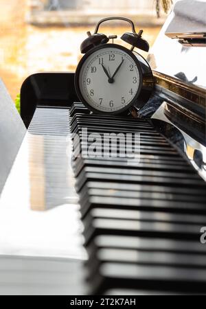 Black alarm clock stand on the Piano Keyboard. Time for music concept. Space for text, Selective focus. Stock Photo