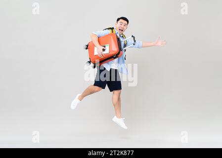 Amazed young Asian tourist man jumping while holding suitcase, boarding pass and passport ready to  fly, studio shot isolated in gray background Stock Photo