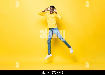 Portrait of happy young African man wearing headphones listening to music and jumping in studio yellow color isolated background Stock Photo