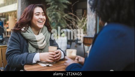 Young multiracial women having coffee break at vintage bar outdoor during winter time - Cozy beverage and lifestyle concept - Focus on asian girl face Stock Photo