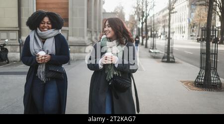 Young multiracial women drinking takeaway coffee walking around the street outdoor during winter time - Cozy beverage and lifestyle concept - Soft foc Stock Photo