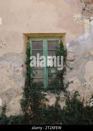 Dilapidated building facade. Cracked and pealed exterior plaster on brick wall and old window frames, no people Stock Photo