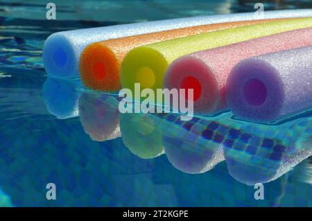 Rainbow coloured pool noodles floating in swimming pool, with reflection in water Stock Photo