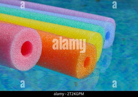 Rainbow coloured pool noodles floating in swimming pool, colourful abstract background with copy space Stock Photo