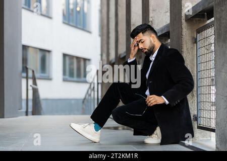 Unhappy sad Indian business man frustrated stress pensive feeling bad after company lost job unemployment problem financial crisis. Arabian Hindu freelancer guy sits at office business center building Stock Photo