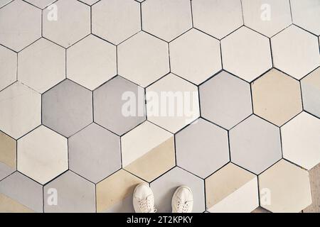 Light-colored sneakers stand on the tile. Finishing the floor with a copy space. The floor is made of light ceramic tiles. Concrete hexagonal paving stones for paving. High quality photo Stock Photo