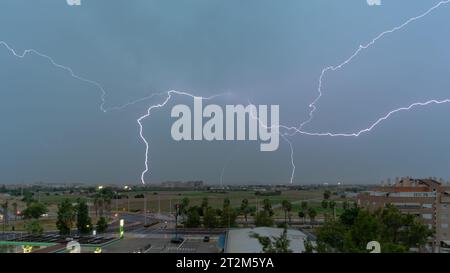 Stormy sky with several huge lightning bolts striking the ground on the outskirts of a city over agricultural fields. Weather concept Stock Photo