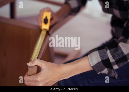 Women measuring length of chair with measure tape while assembling and renovation chair furniture. Stock Photo