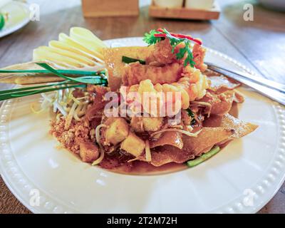 Side view of delicious stir fried crispy wontons with deep fried shrimp, fresh coriander , lemon and bean sprouts in ceramic plate. Thai style phad th Stock Photo
