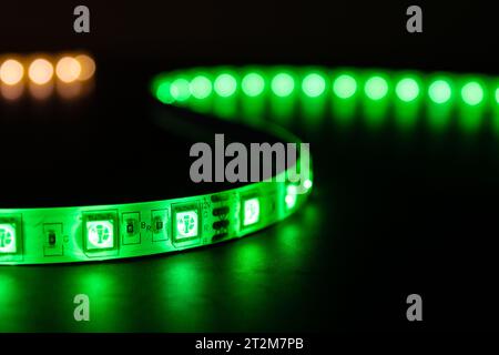 Bobbin with roll of glowing LED strip lighting placed on table, green and warm white color Stock Photo