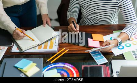 Two creative graphic designers hold color swatches to discussing and sketching to designing project. Stock Photo
