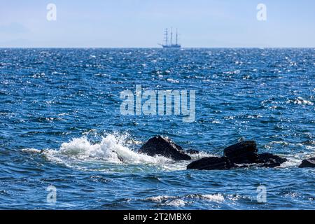 Waves breaking on rocks with the barquentine 'Thalassa' (built 1980) off the coast of the Kintyre Peninsula, Argyll & Bute, Scotland UK Stock Photo