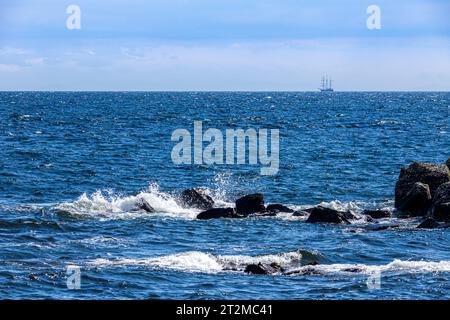 Waves breaking on rocks with the barquentine 'Thalassa' (built 1980) off the coast of the Kintyre Peninsula, Argyll & Bute, Scotland UK Stock Photo