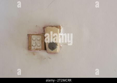damaged and repaired light and ceiling fan switches on a dirty white wall, unprofessional electrician concept with copy space Stock Photo