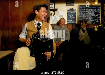 Traditional folk music UK 1980s. Farmers and countrymen gather at the Kings Head, and also know as the Low House pub, in  Laxfield. Traditional story telling, reciting of poetry and folk music songs are performed in an informal manner every Sunday morning. A local farmer playing a melodeon. Laxfield, Suffolk, England  1985. 1980s HOMER SYKES Stock Photo