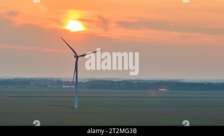 Lone wind turbine in field with orange sun over it at sunset aerial Stock Photo