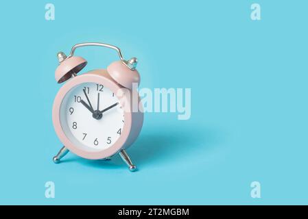 Close up one small pink metal twin bell retro alarm clock over light blue background with copy space, low angle front view Stock Photo
