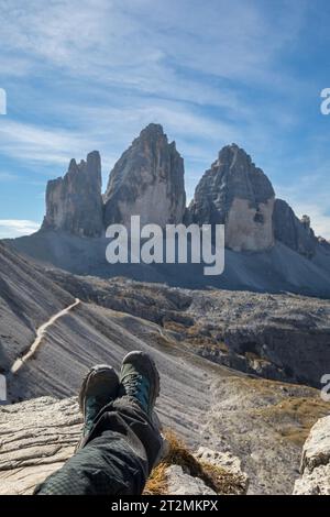 Legs of a hiker lying on the rock enjoying the view on the famous Tre Cime di Lavaredo, Drei Zinnen, Dolomites, Italy Stock Photo