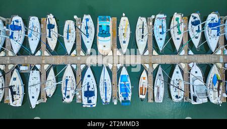 Variety of boats and yachts docked at pier in aerial straight down shot of teal ocean water Stock Photo