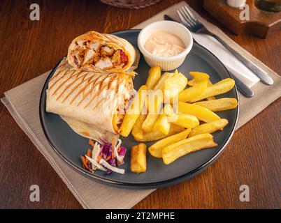 Tortilla wrap with fried chicken meat and vegetables served with French fries Stock Photo