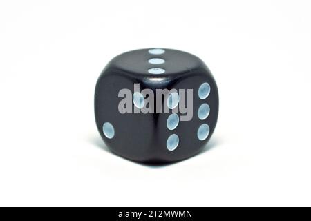 Close up of a black die or dice with bluish coloured spots, isolated against a white background. Stock Photo