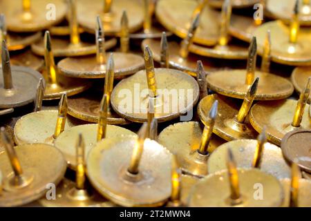 Close up of a random cluster of brass drawing pins, push pins or thumb tacks, the points all facing upwards. Stock Photo
