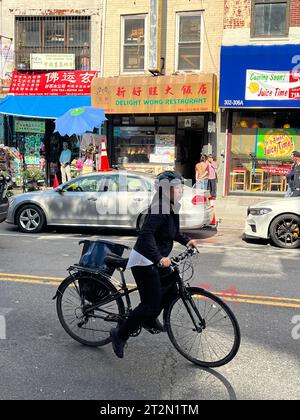 Chinese woman on her bike along Grand Street on the Lower East Side in Manhattan, NYC. Stock Photo