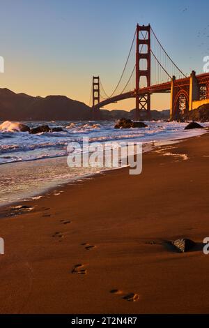 Footprints on beach coming from crashing waves at sunset with Golden Gate Bridge Stock Photo