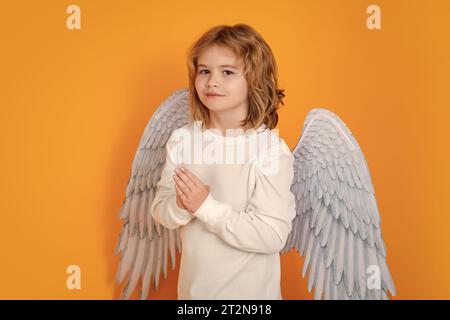 Angel prayer kids. Kid wearing angel costume white dress and feather wings. Innocent child Stock Photo