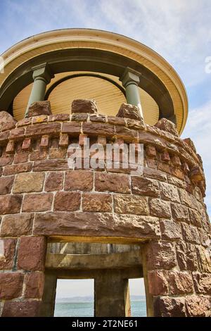 Brown stone tower with circular ceiling under cloudy blue sky and ocean through window Stock Photo