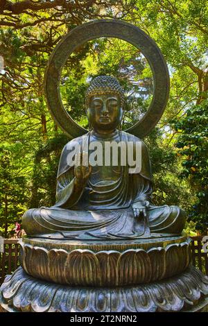 Buddha statue with palm raised and green nature garden behind it Stock Photo