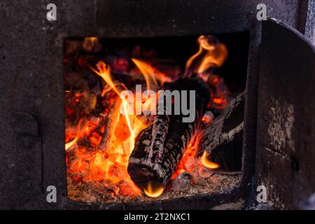 A close up of burning wood in an old stove. The wood is charred and surrounded by red embers and flames Stock Photo